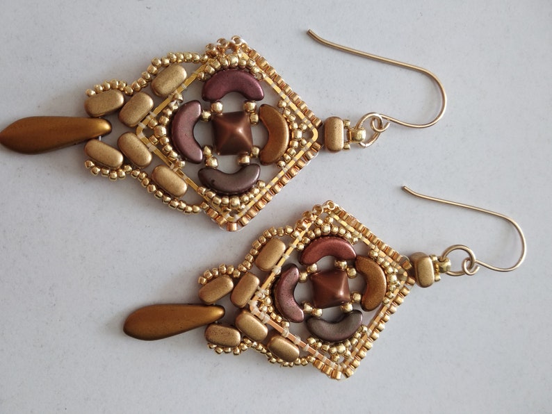 May include: A pair of gold and brown beaded earrings with a geometric design. The earrings are dangle style and have a teardrop-shaped bead at the bottom.