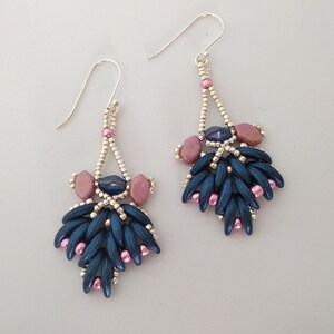 May include: A pair of dangle earrings with a silver wire and blue and pink beads. The earrings have a teardrop shape and are made with a variety of beads, including small round beads, larger oval beads, and long, thin beads.