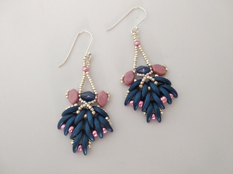 May include: A pair of dangle earrings with a silver wire and blue and pink beads. The earrings have a teardrop shape and are made with a variety of beads, including small round beads, larger oval beads, and long, thin beads.
