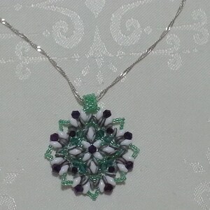 Może przedstawiać: Srebrny łańcuszek z naszyjnikiem w kształcie płatka śniegu z zielonych, białych i fioletowych koralik&oacute;w.
