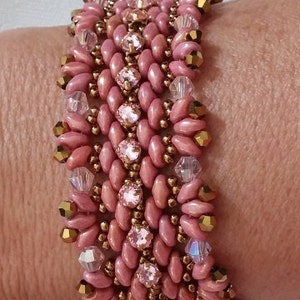 Puede incluir: Un brazalete de cuentas rosa y dorado con un dise&ntilde;o tejido. El brazalete est&aacute; hecho con cuentas peque&ntilde;as y redondas y presenta un acento de cristal.