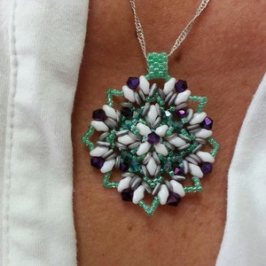 Może przedstawiać: Srebrny łańcuszek z wisiorem w kształcie płatka śniegu z zielonych, białych i fioletowych koralik&oacute;w.