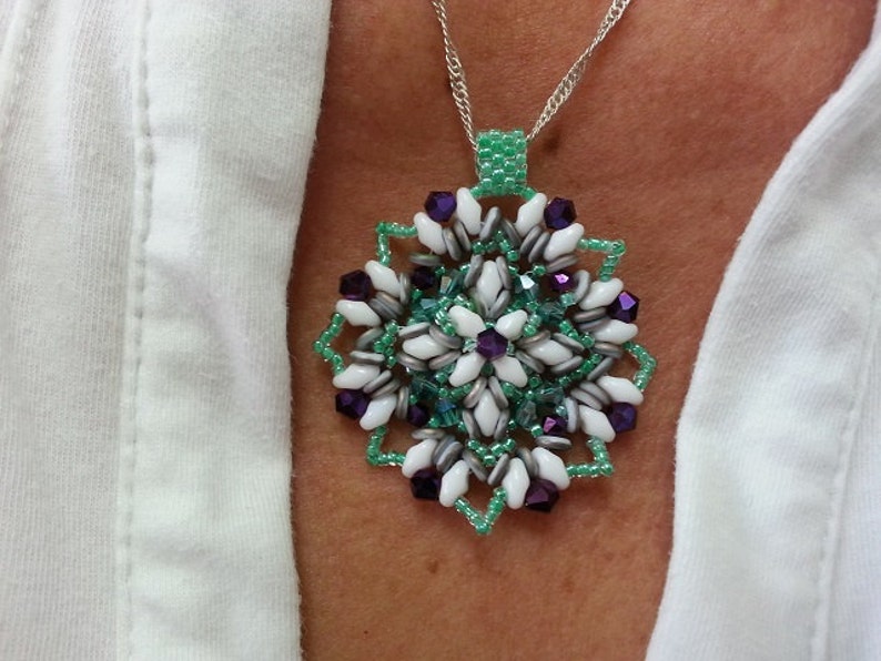 Może przedstawiać: Srebrny łańcuszek z wisiorem w kształcie płatka śniegu z zielonych, białych i fioletowych koralik&oacute;w.