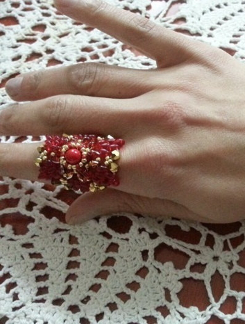 May include: A red and gold beaded ring with a large red gemstone in the center.