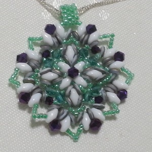 Może przedstawiać: Naszyjnik z białym i srebrnym wisiorem z koralik&oacute;w, z zielonymi i fioletowymi koralikami w kształcie płatka śniegu.