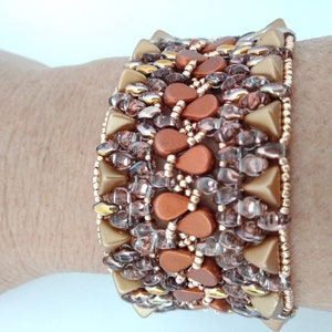 Puede incluir: Un brazalete de cuentas con un diseño geométrico con cuentas de color dorado y cobre.
