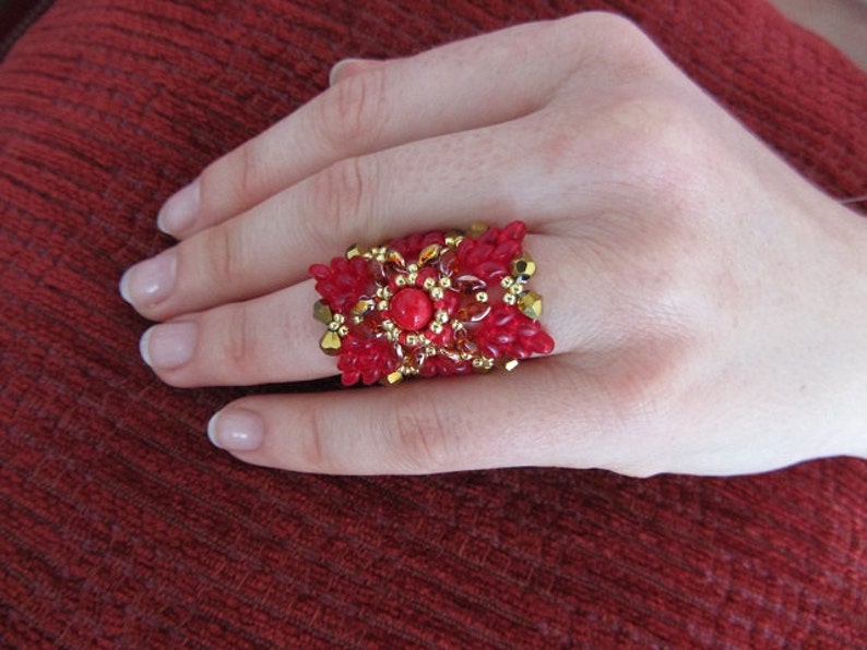 May include: A red and gold beaded ring with a large red gemstone in the center.
