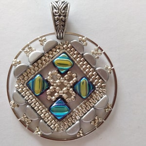 May include: A silver pendant with a circular frame and a beaded design in the center. The beads are silver, gold, and iridescent blue and green. The pendant has a silver bail.