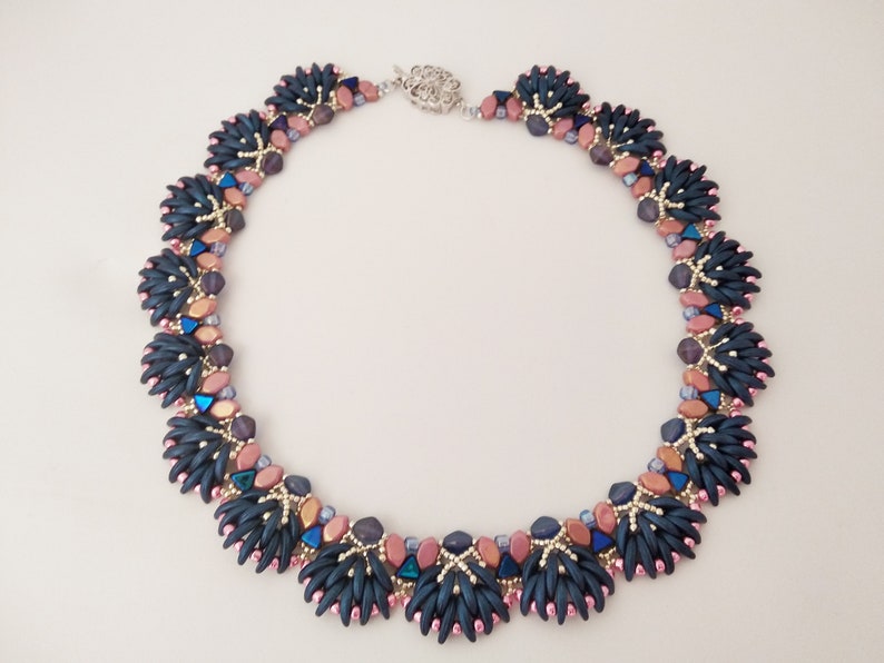 May include: A beaded necklace featuring a dark blue, pink and copper colour scheme. The necklace is crafted from small, faceted beads arranged in a geometric design.
