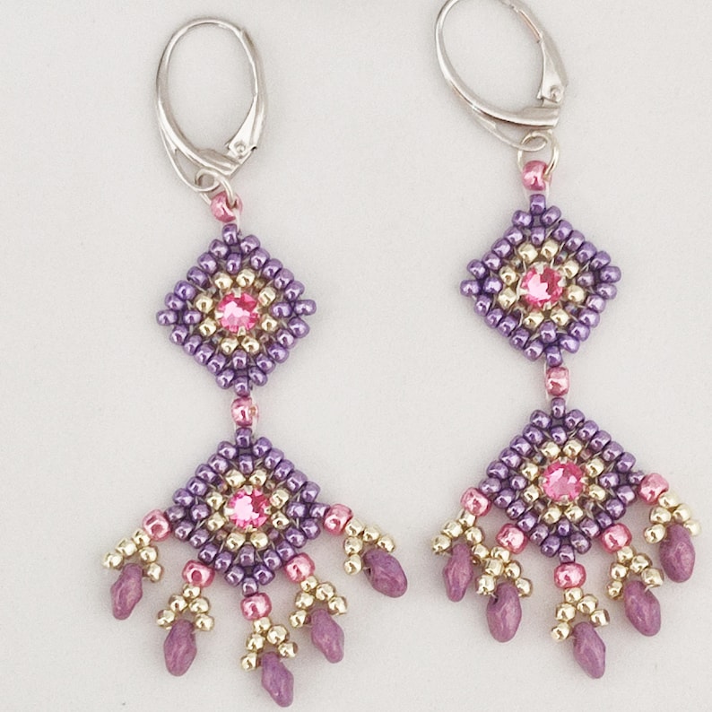 K&ouml;nnte beinhalten: Lila und goldene Perlenohrringe mit rosa Kristall-Akzenten. Die Ohrringe haben eine baumelnde Diamantform mit einer kleineren Diamantform darunter.