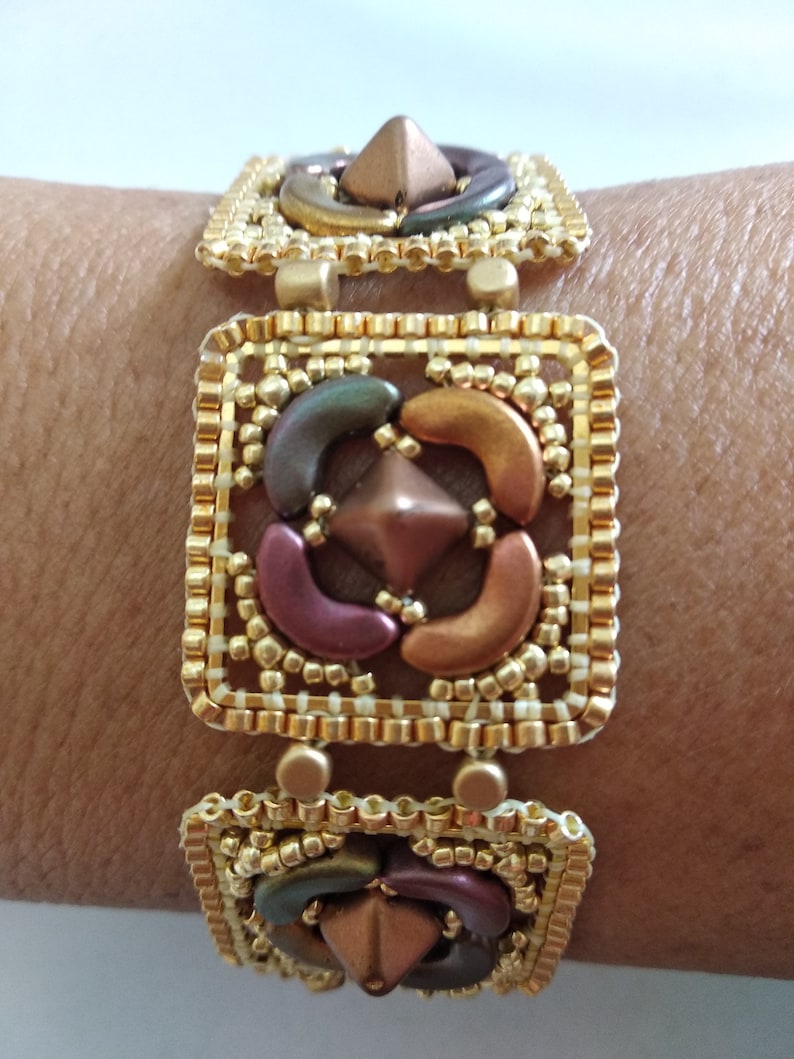 Peut inclure: Un bracelet en perles dor&eacute;es avec un motif carr&eacute; pr&eacute;sentant un motif central de perles brunes, vertes et violettes. Le bracelet a un motif g&eacute;om&eacute;trique et est fait de mat&eacute;riaux de haute qualit&eacute;.