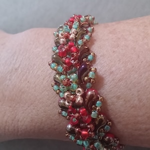 Op de afbeelding: Een kralenarmband met een veelkleurig ontwerp in tinten rood, groen, bruin en goud.