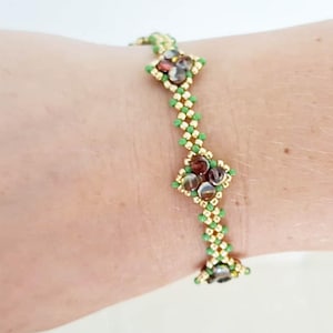 May include: A beaded bracelet featuring a repeating pattern of green and gold beads, with clusters of brown and clear beads. The bracelet is worn on a wrist, showcasing its intricate design and color palette.