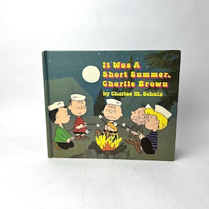 May include: A vintage hardcover book titled "It Was A Short Summer, Charlie Brown" by Charles M. Schulz. The cover features a nighttime campfire scene with cartoon characters. The book is in good condition.