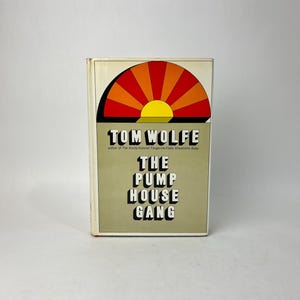May include: A hardcover book titled "The Pump House Gang" by Tom Wolfe. The cover features a stylized sunburst design in orange, red, and yellow above the author's name. The book's title is in bold, black letters on a tan background.