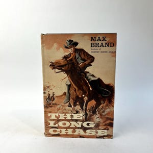 May include: Vintage book cover for "The Long Chase" by Max Brand. The cover features a cowboy on a brown horse, with a sepia-toned background. The title and author's name are prominently displayed.