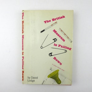 May include: The cover of a book titled "The British Museum is Falling Down" by David Lodge. The cover features a white background with a red and pink title and text. There are three safety pins and two thermometers on the cover.