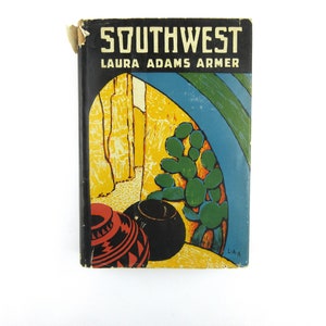 May include: A vintage book cover with the title "SOUTHWEST" by Laura Adams Armer. The cover features a colorful illustration of a desert landscape with cacti, pottery, and a blue sky.