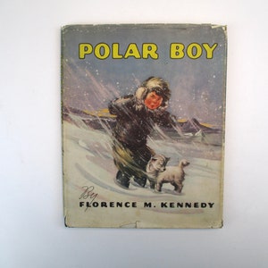 May include: A vintage book cover with a colorful illustration of a young boy in a fur-lined coat and a small white dog standing in a snowy landscape. The title "POLAR BOY" is printed in yellow letters on the cover. The book is by Florence M. Kennedy.