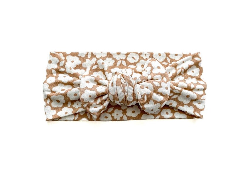 May include: A brown headband with a white floral pattern. The headband is tied in a knot at the top.