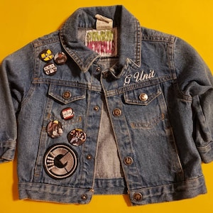 May include: A blue denim jacket with various band and music-themed patches, including Run DMC, Wu-Tang Clan, and G-Unit. The jacket has a white embroidered G-Unit logo on the left chest.