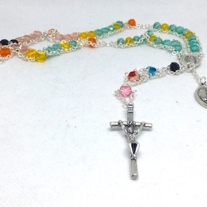 May include: A colorful rosary with a silver crucifix and pendant. The beads are various colors, including pink, yellow, green, and orange. The rosary is made of glass beads and silver chain.