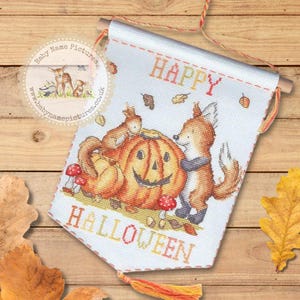 May include: A cross-stitched Halloween banner featuring a carved pumpkin, a fox, and two squirrels. The banner reads "HAPPY HALLOWEEN" in orange and yellow letters. The banner is white with a wooden dowel at the top and a tassel at the bottom.