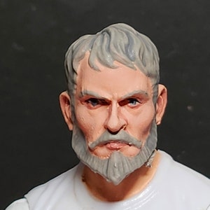 Peut inclure: Gros plan sur une tête de figurine d'action en plastique peinte avec des cheveux gris, une barbe grise et une expression sérieuse.