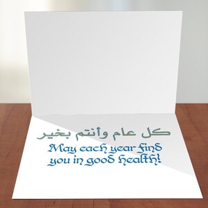 May include: A white card with a blue and green message that says "May each year find you in good health!" in English and "كل عام وانتم بخير" in Arabic.
