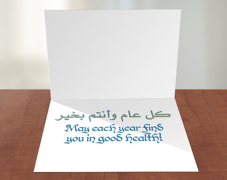 May include: A white card with a blue and green message that says "May each year find you in good health!" in English and "كل عام وانتم بخير" in Arabic.