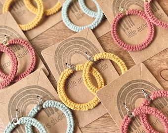May include: A set of six pairs of crocheted hoop earrings in various colors, including yellow, green, and red. The earrings are displayed on cards with the text "little arcoiris studio".