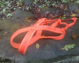 May include: Orange dog harness with adjustable straps and a buckle closure. The harness is made of a soft, comfortable material and is designed to fit snugly around the dog's chest and shoulders.