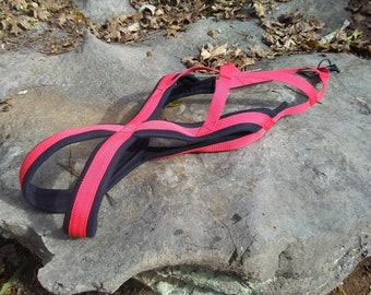 May include: A red and black dog harness with adjustable straps. The harness is made of nylon and has a padded chest piece for comfort.