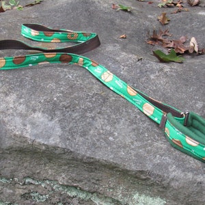 May include: Green and brown dog leash with a pattern of Girl Scout cookies. The leash is made of fabric and has a brown leather handle.