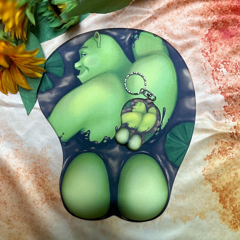 May include: Green Shrek character mousepad with a key chain attached. The mousepad has a black background with green lily pads and a green swamp-like liquid. The key chain is a green Shrek character with a silver key ring.