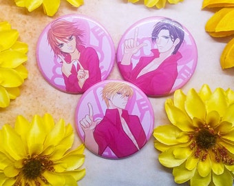 May include: Three pink button pins with anime characters. Each pin features a different character with pink hair, black hair, and blonde hair. The characters are all wearing pink shirts and have a pink background.