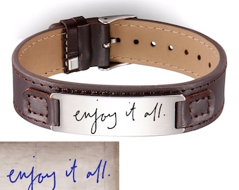May include: Brown leather bracelet with a silver plate engraved with the handwritten text "enjoy it all."