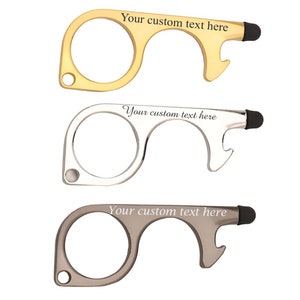May include: Three metal no-touch tools in gold, silver, and grey. Each tool has a large circular opening, a hook, and a stylus tip. The text "Your custom text here" is engraved on each tool.