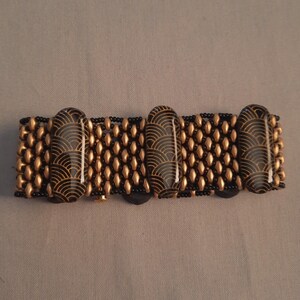 May include: A black and gold beaded bracelet with large black and gold patterned beads. The bracelet is made with small black beads and larger gold beads.