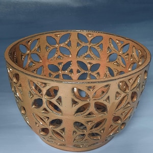 May include: A handcrafted ceramic bowl with a floral cut-out design. The bowl is a warm, earthy tone with a glossy finish. The intricate pattern creates a play of light and shadow, enhancing its decorative appeal. This unique piece is perfect for home decor.