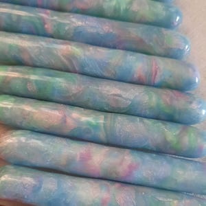 May include: A set of 10 iridescent blue, green, and pink marbled polymer clay knitting needles. The needles are arranged in a stack, with the tips of the needles facing the viewer.