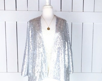 May include: A silver sequined cardigan with a long, open front and 3/4 sleeves. The cardigan is draped over a white mannequin.