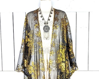 May include: Black sheer kimono with gold sequins and fringe. The kimono is on a white mannequin and has a silver necklace with a large pendant.