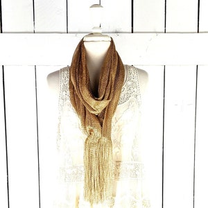 Peut inclure: Un foulard métallique doré avec un pompon à franges sur un haut en dentelle blanche.