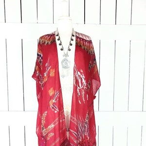 Könnte beinhalten: Ein rotes, durchsichtiges Kimono mit floralem und geometrischem Muster und Fransenbesatz. Das Kimono befindet sich auf einer weißen Puppe.