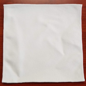 Puede incluir: Un paño de limpieza de microfibra blanco con un borde cosido.