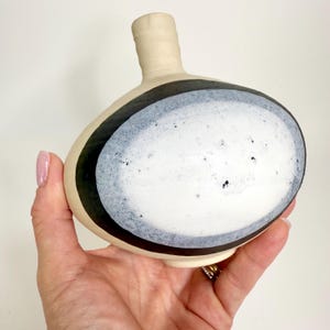 May include: A white ceramic vase with a black and white geometric design. The vase has a round body and a narrow neck.