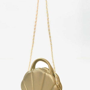 Könnte beinhalten: Eine goldfarbene Handtasche in Form einer Muschel mit einem goldenen Kettenriemen.