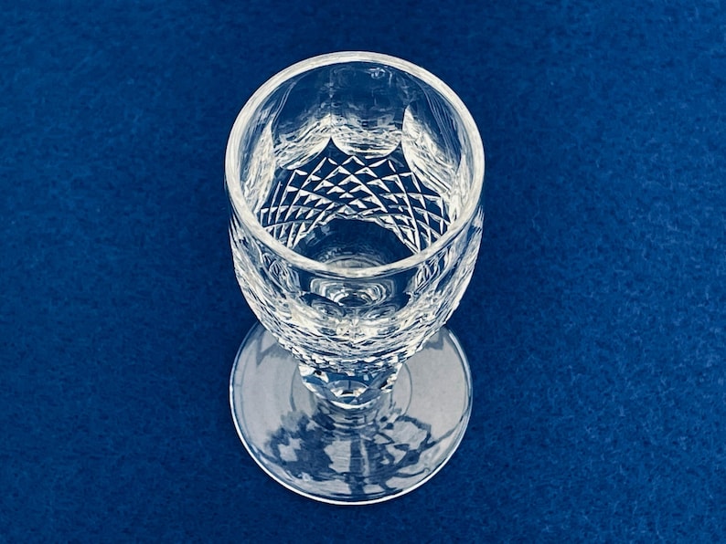 May include: A clear, cut crystal wine glass with a round base and a diamond pattern on the bowl. The glass is set against a deep blue background, showcasing its intricate design and clarity.