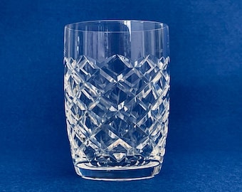 Op de afbeelding: Een helder drinkglas van kristal met een diamantgeslepen patroon. Het glas is ongeveer 15 cm hoog en heeft een stevige basis. De blauwe achtergrond accentueert het ingewikkelde patroon.